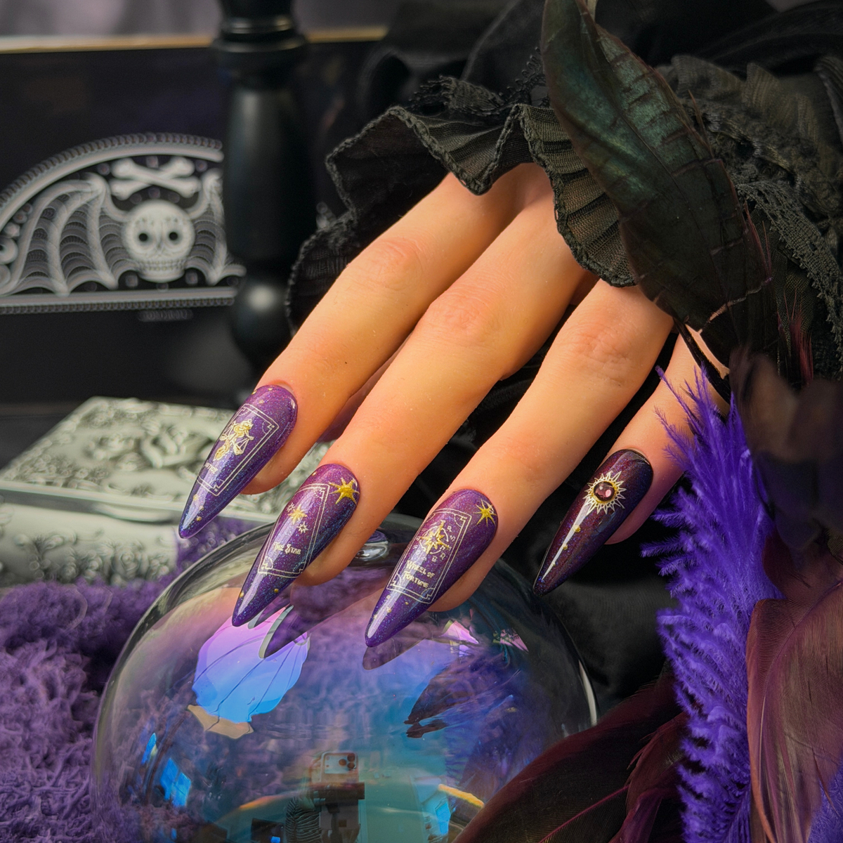 a set of press on nails painted with a purple background and gold tarot card designs, resting on a crystal ball